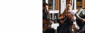 Drei Musiker mit Saiteninstrumenten vor einem Lokal