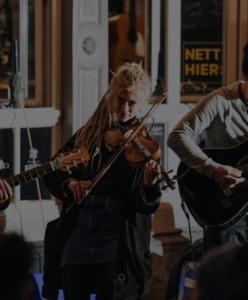 Drei Musiker mit Saiteninstrumenten vor einem Lokal