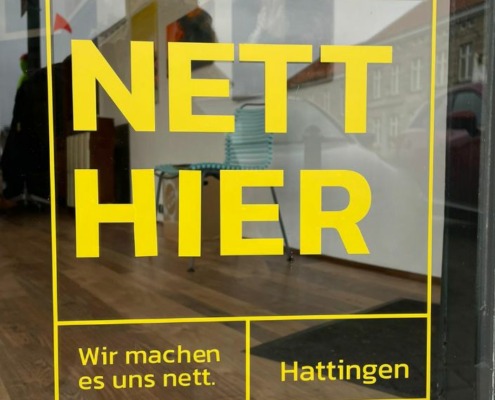 Ein gelber Aufkleber mit dem Slogan "Nett hier" auf einem Schaufenster